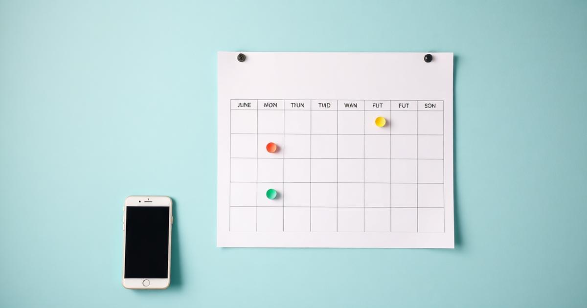 Calendário de parede com marcadores coloridos indicando datas de vencimento ao lado de um celular